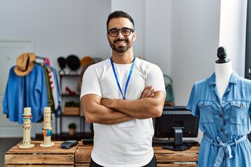 Young hispanic man shopkeeper smiling confident standing with arms crossed gesture at clothing store