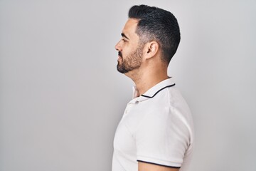 Young hispanic man with beard wearing casual clothes over white background looking to side, relax profile pose with natural face and confident smile.