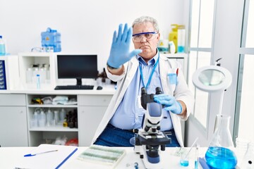Senior caucasian man working at scientist laboratory doing stop sing with palm of the hand. warning expression with negative and serious gesture on the face.