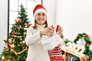 Middle age caucasian woman smiling confident inserting gift on christmas sock at home