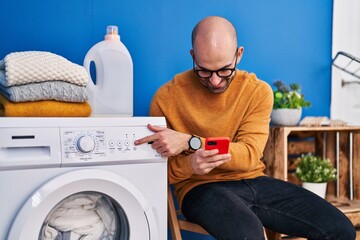 Young man using smartphone turning on washing machine at laundry room