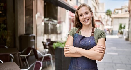 Young blonde woman smiling happy wearing apron at coffee shop