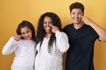 Family of mother, daughter and son standing over yellow background pointing with hand finger to face and nose, smiling cheerful. beauty concept