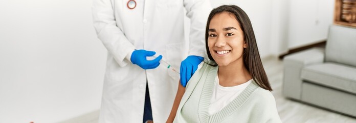 Doctor injecting covid-19 vaccine to latin woman at clinic.