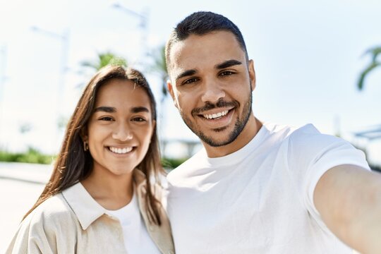 Young latin couple smiling happy and hugging making selfie by the camera at the city.