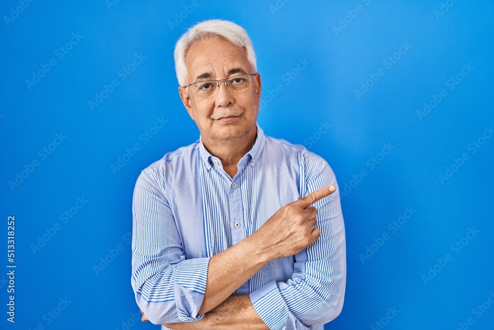 Canvas Prints Hispanic senior man wearing glasses pointing with hand finger to the side showing advertisement, serious and calm face