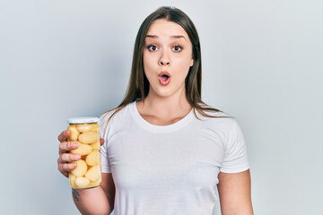 Young hispanic girl holding bottle with boiled potatoes scared and amazed with open mouth for surprise, disbelief face