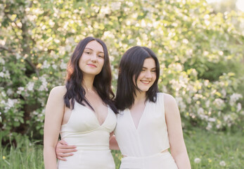 two young girls in white dress on background flowering apple tree