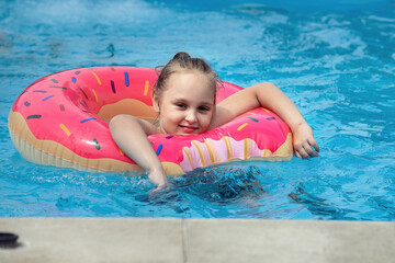 an eight-year-old girl has fun and actively spends her holidays in an outdoor pool in cool water in the summer, she is wearing a bright red inflatable ring