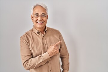 Hispanic senior man wearing glasses cheerful with a smile of face pointing with hand and finger up to the side with happy and natural expression on face