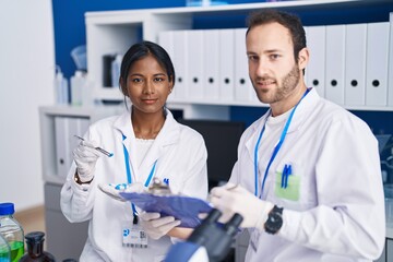 Man and woman scientists holding capsule writing report at laboratory