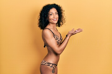 Young latin girl wearing bikini pointing aside with hands open palms showing copy space, presenting advertisement smiling excited happy - Powered by Adobe