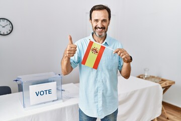 Middle age man with beard at political campaign election holding spain flag smiling happy and...