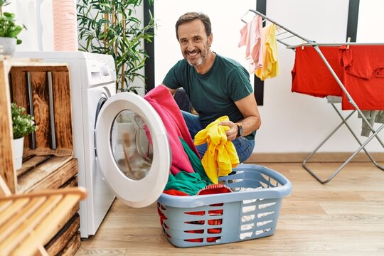 Middle age hispanic man smiling happy doing laundry at home.