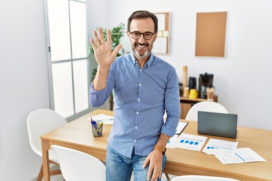 Middle age hispanic man with beard wearing business clothes at the office showing and pointing up with fingers number five while smiling confident and happy.
