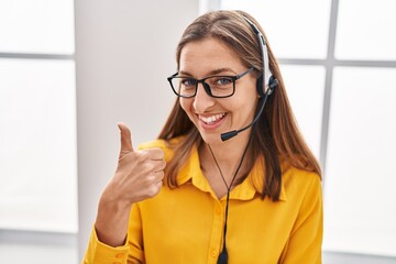 Young woman wearing call center agent headset smiling happy and positive, thumb up doing excellent...