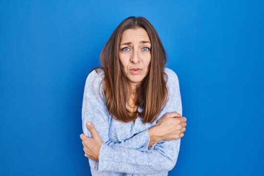 Young Woman Standing Over Blue Background Shaking And Freezing For Winter Cold With Sad And Shock Expression On Face