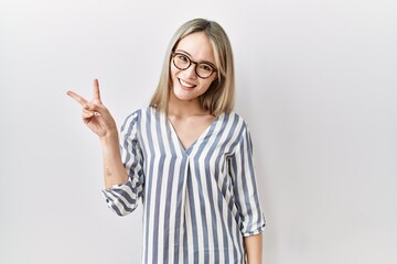 Asian young woman wearing casual clothes and glasses smiling with happy face winking at the camera doing victory sign. number two.