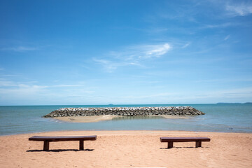 Fototapeta na wymiar Outdoor sunny view of empty wooden bench on a beach against sea and blue sky. 