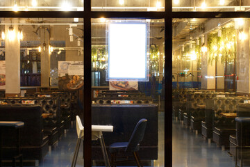 Signboard for advertising behind the stained-glass window of a cafe with bright lights. Empty restaurant at night. Mock-up.