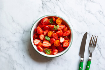 Bowl of tomato cherry and strawberry mix salad on the marble background