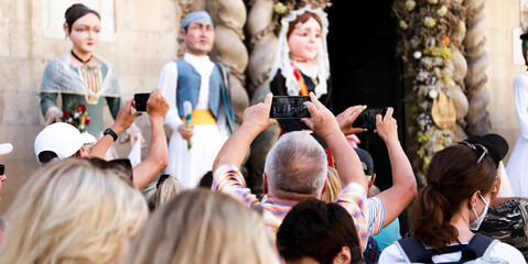 tourists and people from Alicante watching and recording with their mobile phones the parades and...