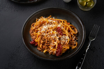Classic pasta Bolognese. Tasty traditional italian dish of fettuccine with tomato and meat mince sauce served in a plate with parmesan cheese on black plate over dark texture background stone or table