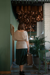 Woman with vintage suitcase in hands in cafe. Tourist lady. Back view. Vertical frame.