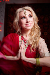 A beautiful European girl looking like an Arab woman in a red room in a harem. Photo shoot of an oriental style odalisque. A model poses in a sari as an indian woman in india