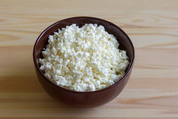 Natural homemade cottage cheese in a bowl on a wooden background. Top view, selective focusing.