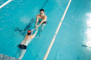 A coach teaches a seven-year-old boy to swim in a modern swimming pool. Learn to swim. Development of children's sports. Healthy parenting and promotion of children's sports.
