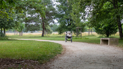 White bear teddy bear sitting on a wheelchair on a green path in a park