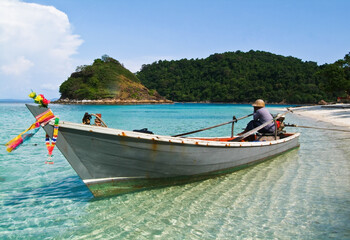 A traditional wooden longtail boat in a clear sea against a blue sky, Thailand.
