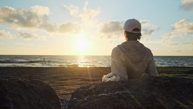 Man on a beach is looking distance during beautiful summer sunset. Human looks to the sun over horizon in  morning while sunrise. Happy person contemplates the beauty of nature. Freedom. Slow motion