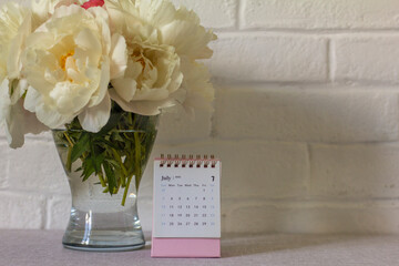 Calendar for July 2022 and peonies on the table. Desktop calendar for planning.