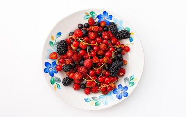 Fresh berries on a plate on a white background, red and black currants and black mulberries, wild strawberries and cherries, top view