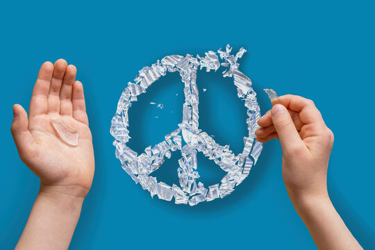 Children's hands close-up without face putting together peace sign or badge from broken glass pieces on blue background. Concept No war, stop hostilities, let there be peace. Copy space.Hope for world