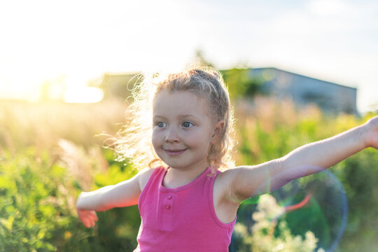 Little joyful blond girl against the background of field grass and sunset
