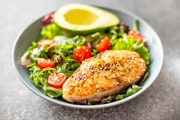 grilled salmon steak and fresh green vegetable tomato salad with lettuce and avocado on stone background