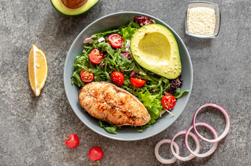 grilled salmon steak and fresh green vegetable tomato salad with lettuce and avocado on stone background