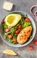 grilled salmon steak and fresh green vegetable tomato salad with lettuce and avocado on stone background