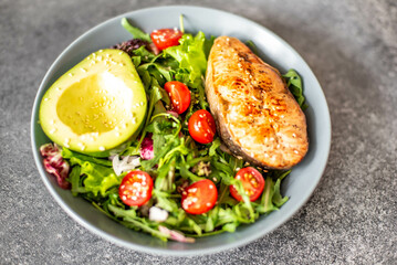 grilled salmon steak and fresh green vegetable tomato salad with lettuce and avocado on stone background