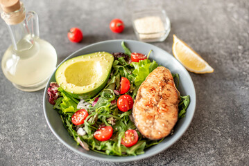 grilled salmon steak and fresh green vegetable tomato salad with lettuce and avocado on stone background
