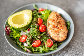 grilled salmon steak and fresh green vegetable tomato salad with lettuce and avocado on stone background