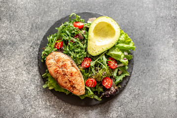 grilled salmon steak and fresh green vegetable tomato salad with lettuce and avocado on stone background