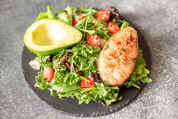 grilled salmon steak and fresh green vegetable tomato salad with lettuce and avocado on stone background