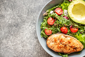grilled salmon steak and fresh green vegetable tomato salad with lettuce and avocado on stone background with copy space for your text