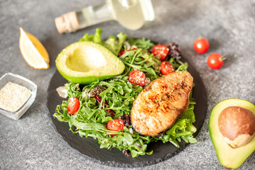 grilled salmon steak and fresh green vegetable tomato salad with lettuce and avocado on stone background