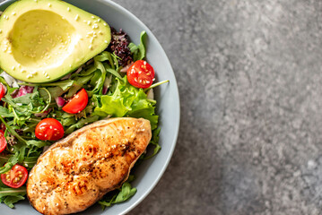grilled salmon steak and fresh green vegetable tomato salad with lettuce and avocado on stone background with copy space for your text
