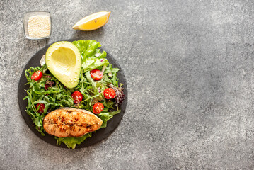 grilled salmon steak and fresh green vegetable tomato salad with lettuce and avocado on stone background with copy space for your text